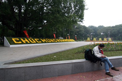 Một du khách người Trung Quốc ngồi cạnh tấm biển chúc mừng năm mới 2012 tại công viên Lê Nin.